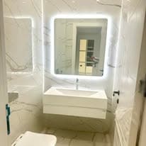 Bathroom with a backlit mirror, marble vanity, and wall-hung basin